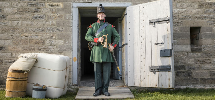 Un homme en costume se tient au garde-à-vous à l’une des portes du fort Wellington 