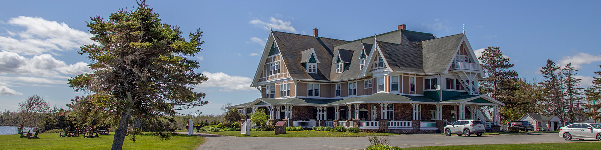 Grande maison de style victorien avec plusieurs pignons et un porche enveloppant sous un ciel bleu avec des nuages épars.