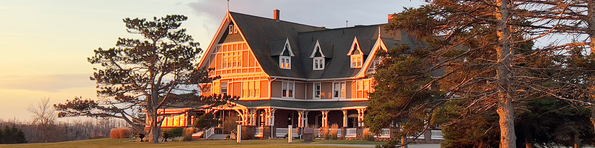 Large Victorian-style house bathed in warm sunset light with tall trees surrounding it