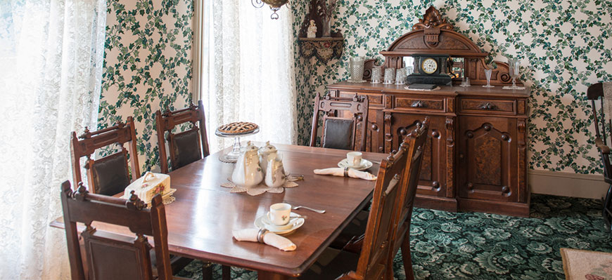 Ensemble de salle à manger antique dans une pièce avec tapis imprimé vert et papier peint à motifs verts. 