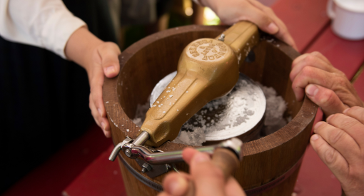 Des mains entourent une baratte à beurre à l'ancienne.