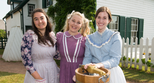 Trois femmes en tenue d'époque se tiennent ensemble devant la maison Green Gables.