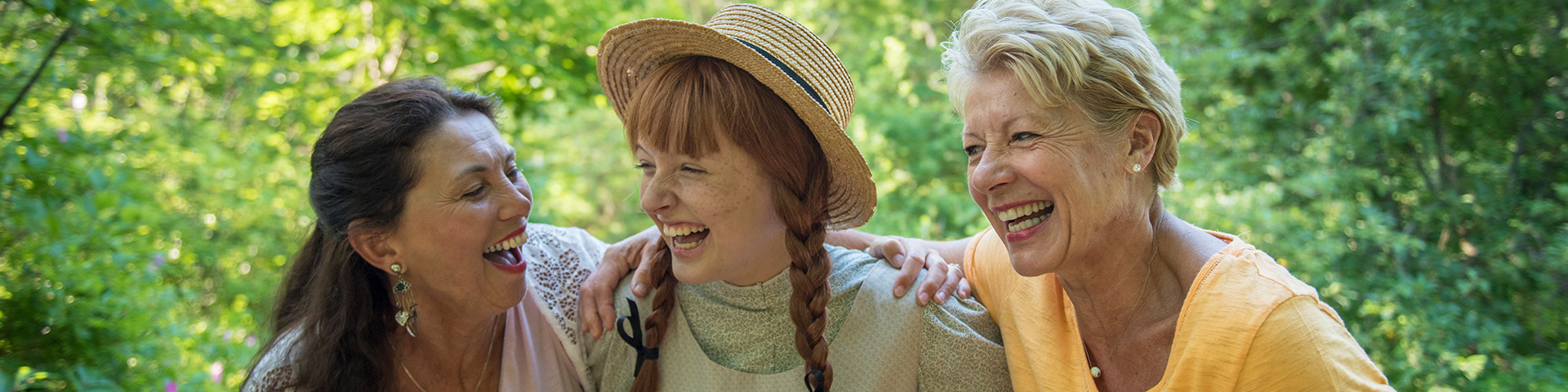 Anne Shirley, personnage costumé, prend du bon temps avec deux visiteurs adultes dans le sentier Balsam Hollow du site patrimonial Green Gables lors d'une journée d'été.