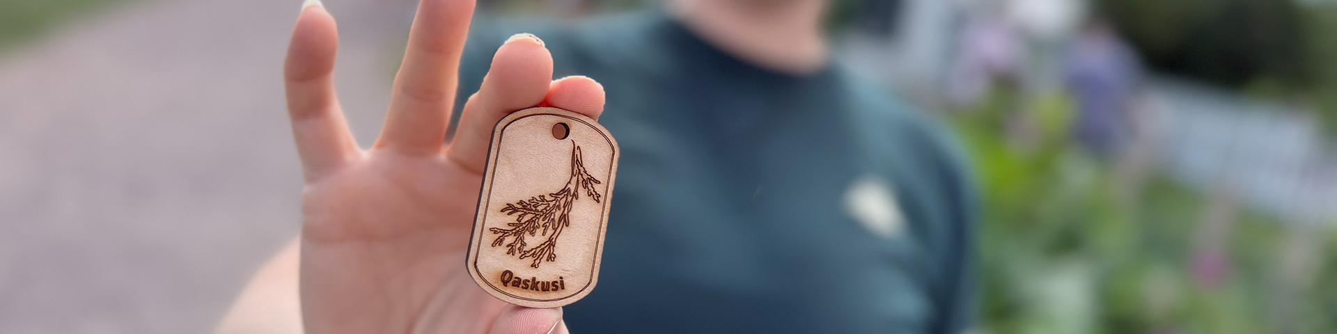 Close up of a small wooden tag with leaves etched on it being held by a Parks Canada staff member.