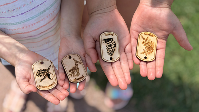 Deux paires de mains tenant quatre petites étiquettes en bois sur lesquelles sont gravés des dessins.