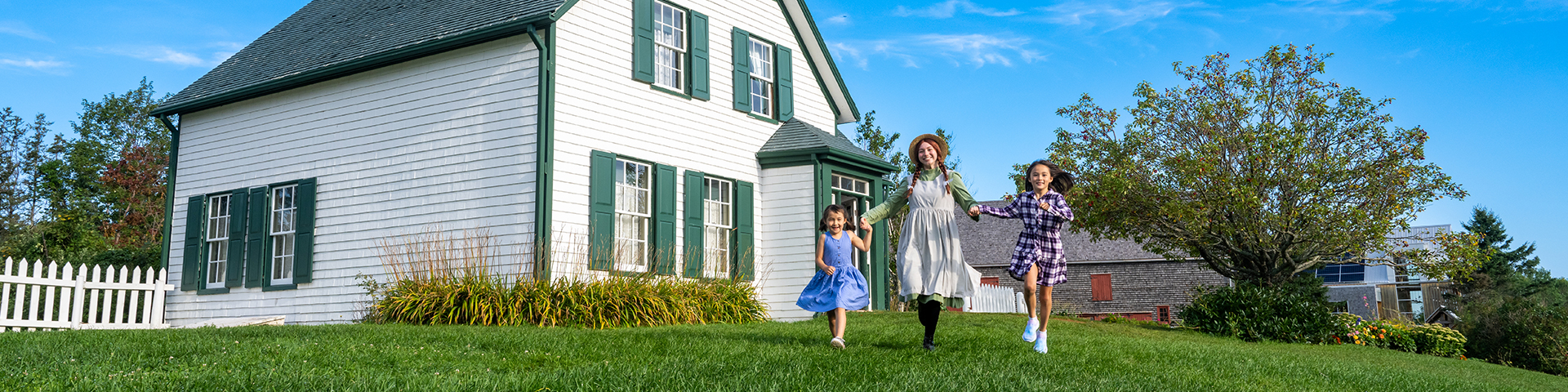 Anne runs across the front lawn of Green Gables house with two young visitors. 