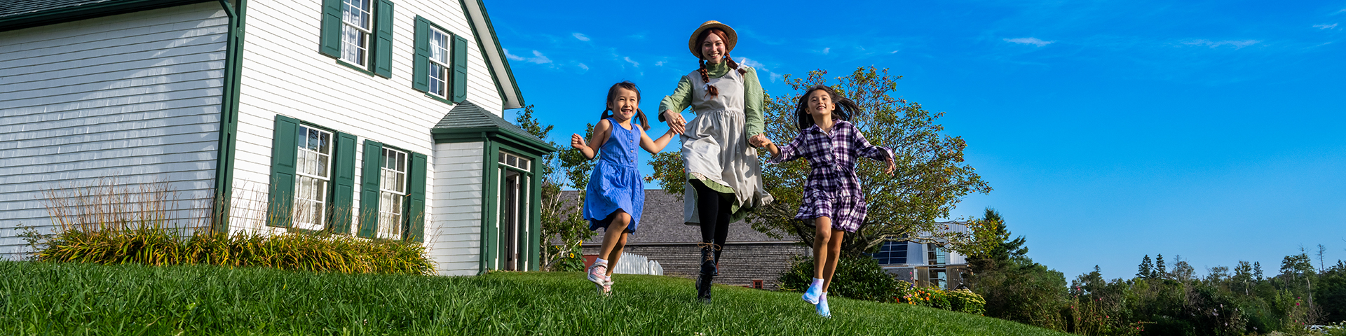 Anne skips across the lawn at Green Gables with two children laughing. 