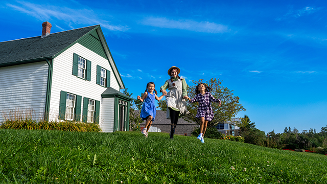 Anne et deux jeunes traversent en courant la cour devant la maison aux pignons verts.