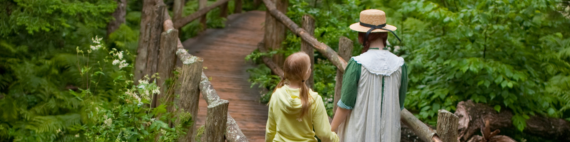 Two youth walking down a wooden bridge surrounded by lush green trees. 