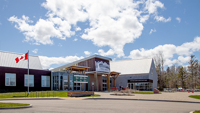 The front side of the Green Gables Visitor Centre depicting the flat parking lot area leading to the main walkway into the building. 