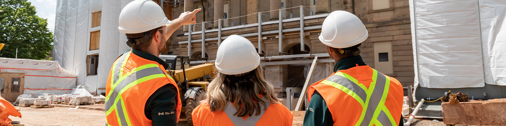 Three people wearing hard hats looking at Province House under construction.