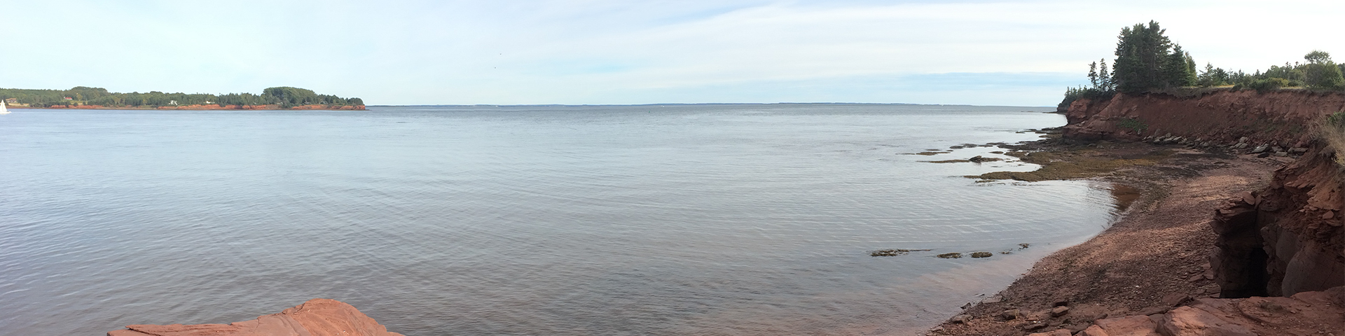 Calm water surrounded by red clay cliffs and green trees and grass on a sunny day.