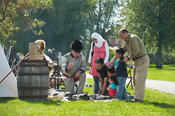 Un interprète en costume et des visiteurs lors de la reconstitution d'un campement datant d'environ 1812 au lieu historique national du Fort-Chambly