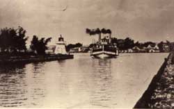 Bateau à vapeur entrant dans la digue Becker. À la gauche, un petit phare. À l'arrière-plan, village de Sainte-Anne-de-Bellevue, 1910.