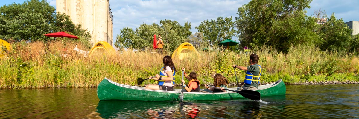 A family and a Parks Canada instructor paddle a canoe in the calm waters of the Lachine Canal.