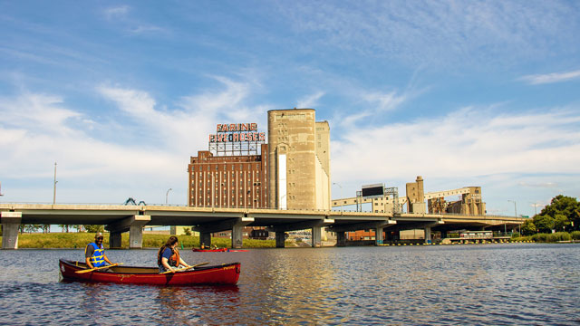 People in a canoe on the Lachine Canal, overlooking the iconic Five Roses flour mill.