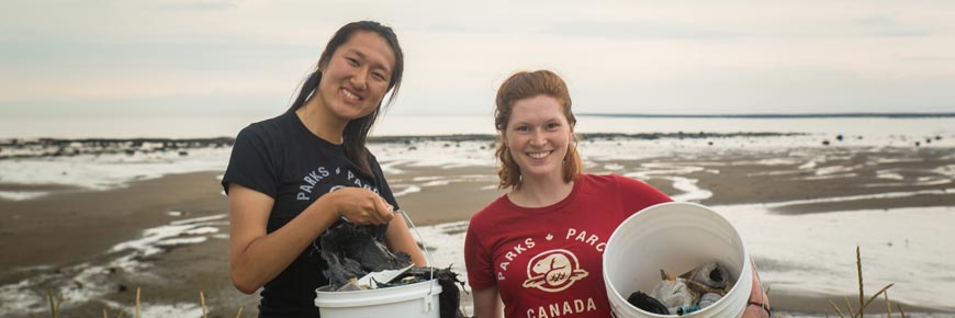 Deux participantes souriantes montrent fièrement les déchets qu'ils ont ramassés dans des seaux en plastique