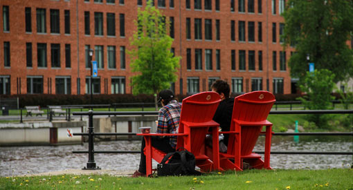 Two people sitting on red chairs at Place des Bassin on the edge of the Lachine Canal