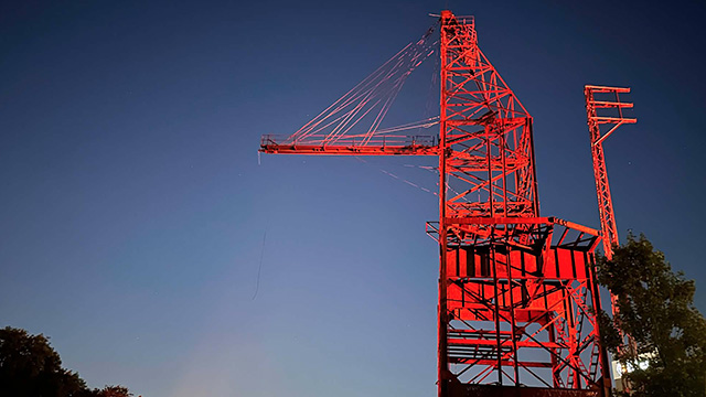 Historic red steel crane illuminated at dusk.