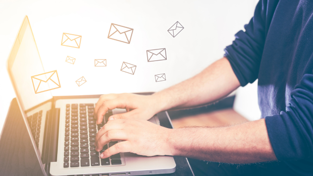 Hands typing on a laptop keyboard. Envelopes floating in the air above the computer.