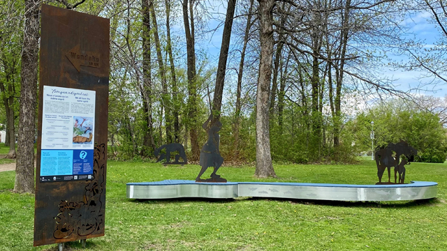 View of a rest area with the steel silhouette of a bear, a hunter, a moose, a steel panel and an aluminum bench at the Cartier-Brébeuf national historic site.