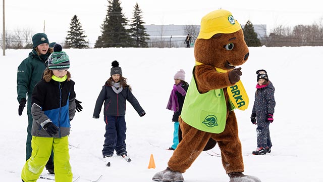 Children learning to cross-country ski with a beaver mascot.