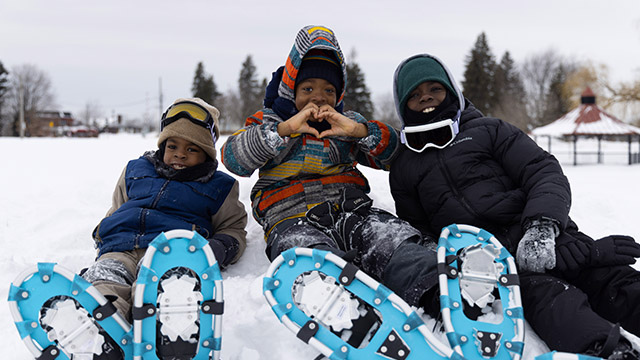 Smiling children, one of them forming a heart with his hands during the winter.