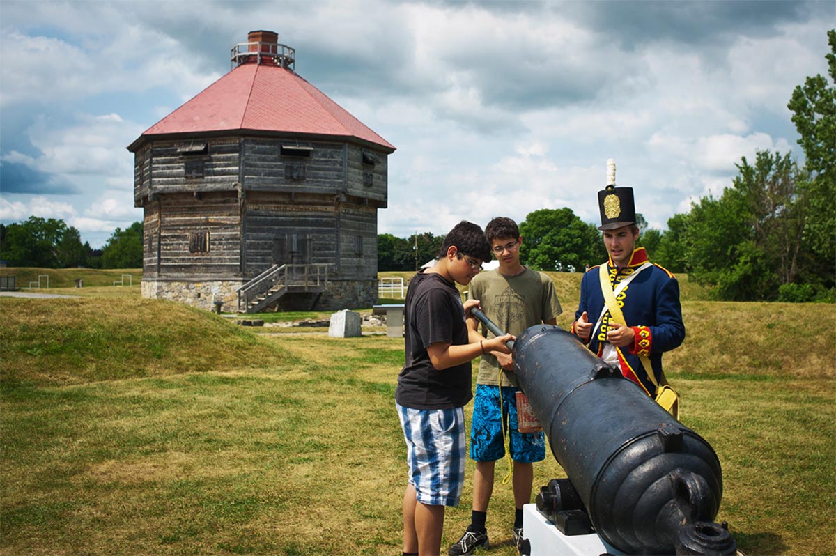 A guide costumes in military uniform shows a cannon to teenagers.