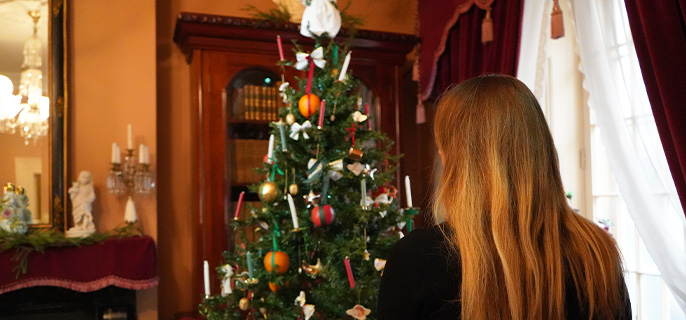 Une dame de dos regarde le sapin de Noël dans le salon principal du lieu historique national de Sir-George-Étienne-Cartier.