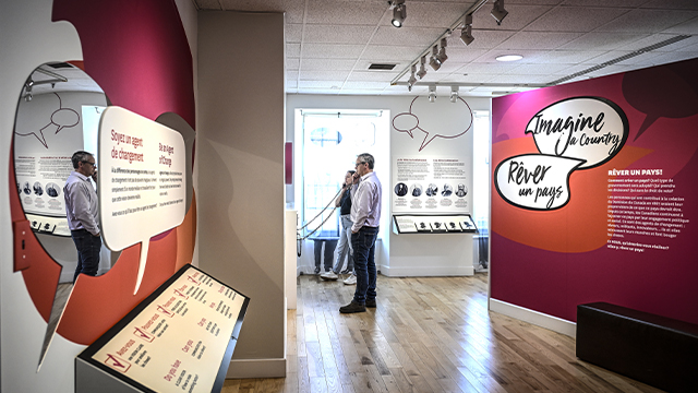 Two visitors, a man and a woman, interact with the audio terminals in the Imagine a Country exhibition, presented at Sir George-Étienne Cartier National Historic Site.