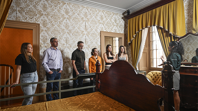 Four adult women and two adult men take a group tour of Madame Cartier's room at Sir George-Étienne Cartier National Historic Site, as a Parks Canada guide explains 19th-century bourgeois traditions and life.