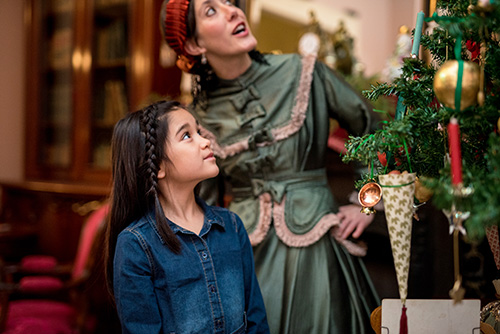A little girl and a costumed guide contemplate an old-fashioned Christmas tree