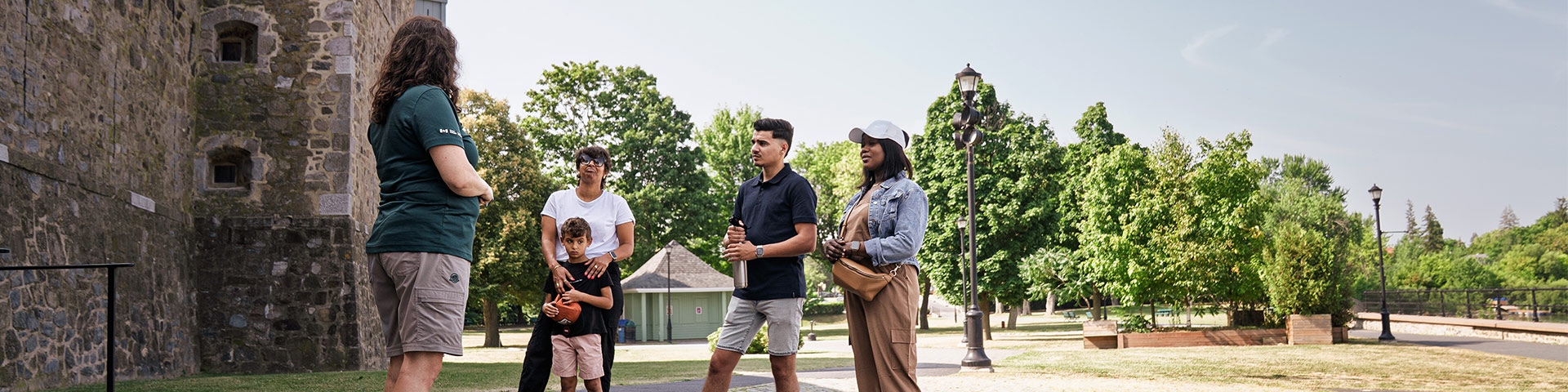 A female Parks Canada guide welcomes four visitors (a woman and her son, and a young couple) in front of the main entrance to Fort Chambly National Historic Site.