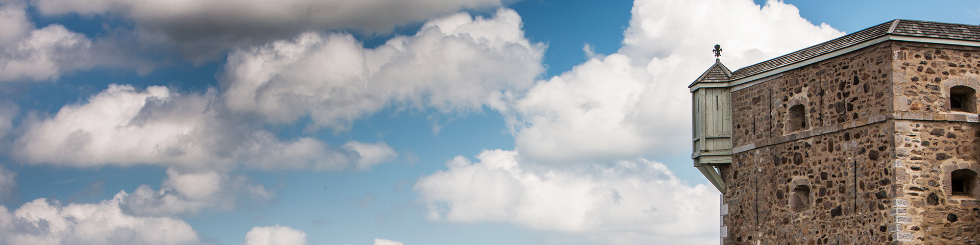 View of a bartizan at Fort Chambly National Historic Site, taken from the southwest, against a backdrop of blue sky and large, puffy white clouds.