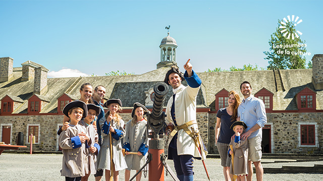 A costumed guide tells the story of Fort Chambly National Historic Site to a family of visitors and children dressed as soldiers in the inner courtyard.