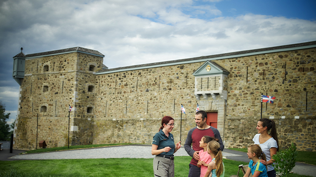 Une guide du lieu historique national du Fort-Chambly explique l’histoire du fort à une famille de deux adultes et trois enfants.