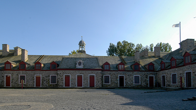 Exterior summer photo of the open courtyard of Fort Chambly National Historic Site, showing the fort's stone façade and numerous doors.