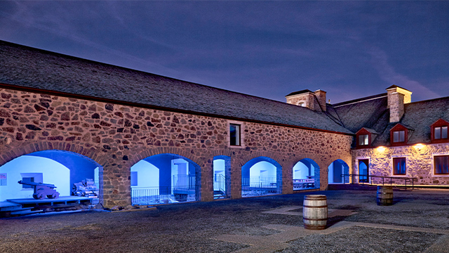 Exterior photo of the open courtyard of Fort Chambly National Historic Site, showing the arcades lit up at night.