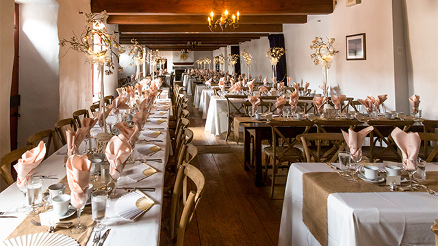  Photo of the Salle Jacques-de-Chambly, located in Fort Chambly National Historic Site, where you can see numerous decorated wooden tables and banquet chairs during a wedding.