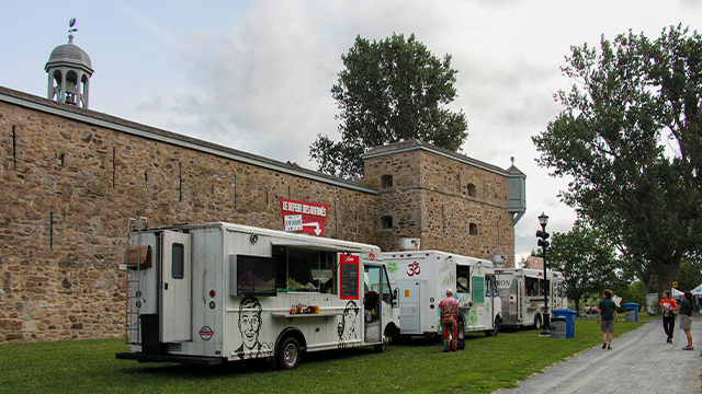 Outdoor summer photo of Fort Chambly National Historic Site Park, featuring street food trucks and the fortification during a festival.