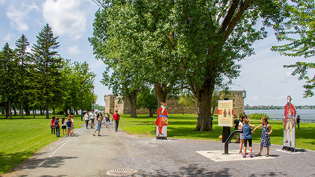 Outdoor summer photo of Fort Chambly National Historic Site Park, showing trees, several pedestrians and the fortification.