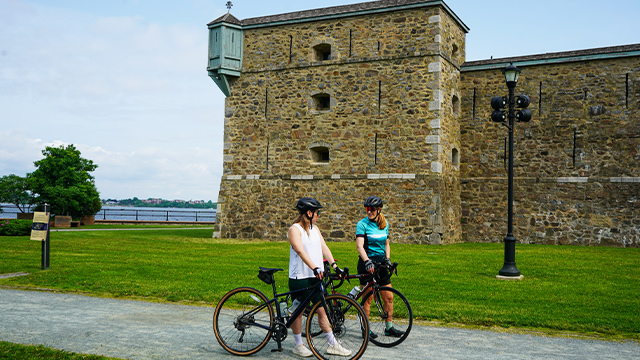 Two female cyclists take a break in front of the Fort Chambly National Historic Site on a beautiful summer day.