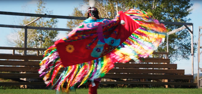 Une jeune fille autochtone vêtue d’une régalia effectue une danse traditionnelle à l’extérieur.