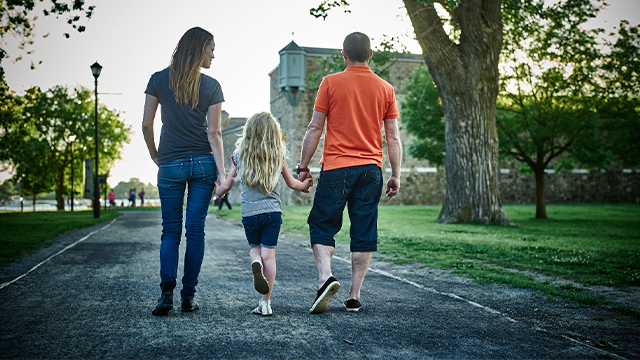 One family, including a man, a woman, and a young girl, are walking along a gravel path toward Fort Chambly in the early evening during the summer.