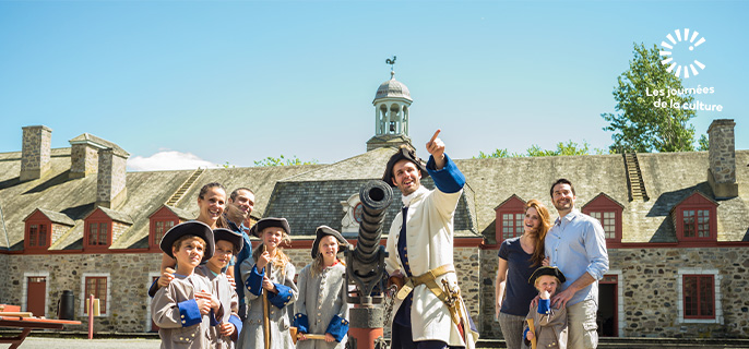 A costumed guide tells the story of Fort Chambly National Historic Site to a family of visitors and children dressed as soldiers in the inner courtyard.