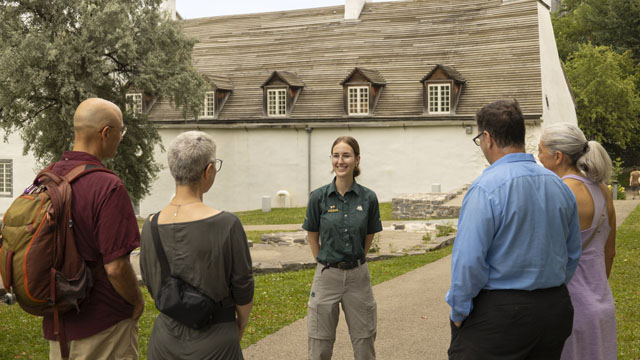 A Parks Canada guide is giving a guided tour to a group of 4 adults at Artillery Park opposite the Dauphine Redoubt.