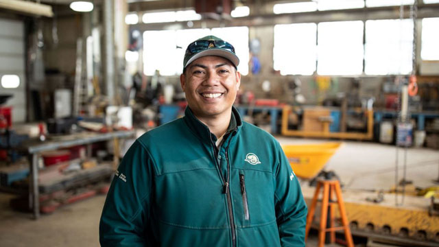  A smiling Parks Canada employee poses in the foreground in a carpentry workshop.