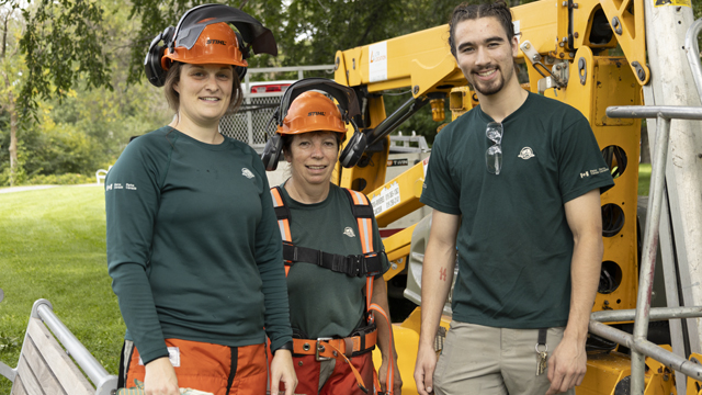 Three members of the Parks Canada technical services team at the Cartier-Brébeuf National Historic Site in front of machinery.