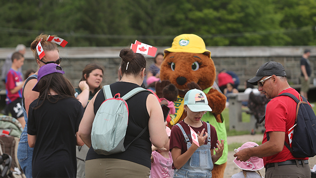Un groupe de visiteurs portant des petits drapeaux du Canada entourant la mascotte Parka au fort Numéro-Un.