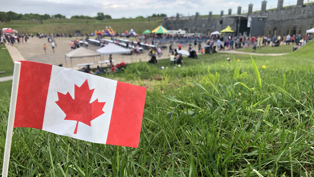Un drapeau canadien est en avant-plan devant la champ de parade du fort Numéro-Un lors des festivités de la Fête du Canada.